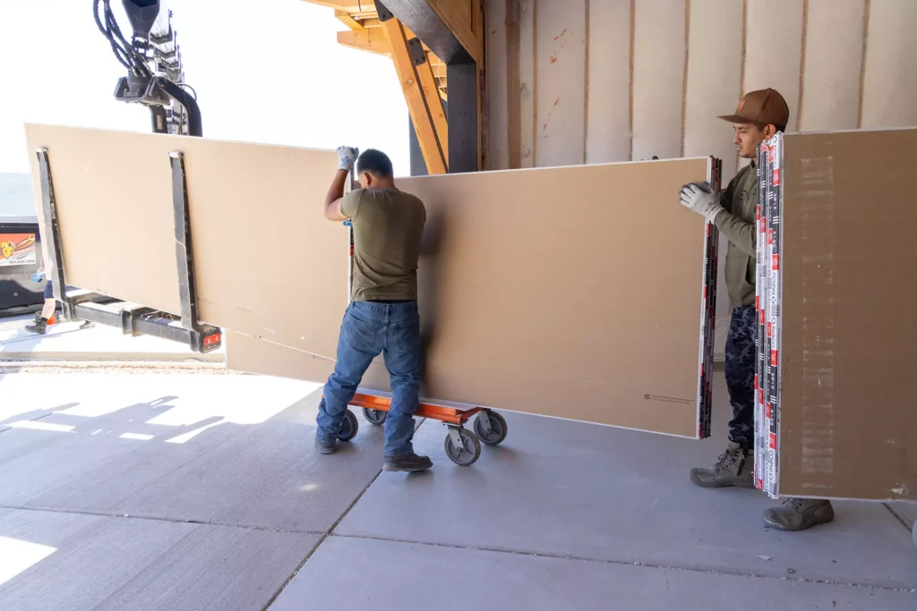Colonial delivery crew carrying drywall sheets into a home under construction