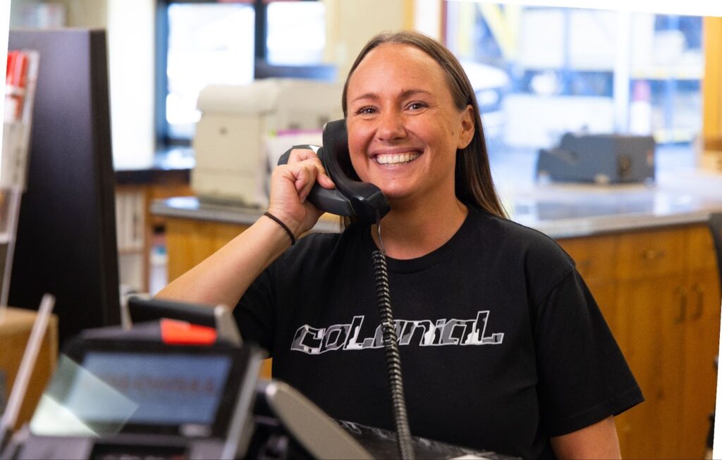 Smiling Colonial Building Supply team member answering the phone at the sales counter in the showroom/office.