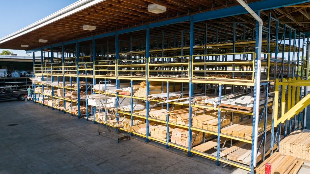 Covered lumber storage racks with stacked boards and sheet goods at Colonial Building Supply in Centerville, Utah.